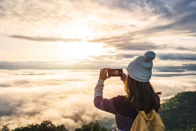 Rear view of woman photographing against sky during sunset