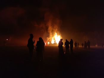 Silhouette people standing by bonfire at night