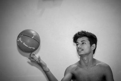 Portrait of young man playing with ball against wall
