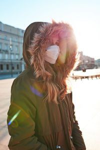 Teenager wearing mask and fur coat in city during winter