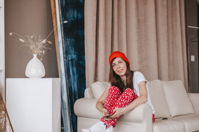 Smiling girl in a red hat and christmas pajamas sitting on the couch. holidays for christmas. 