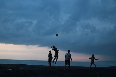 People playing with ball on beach against sky during sunset