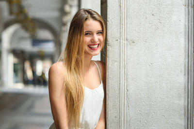 Portrait of smiling young woman leaning on column in corridor