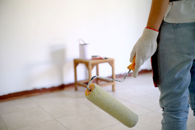 Close-up of woman holding paint roller while standing against wall