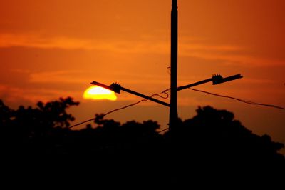 Low angle view of silhouette power lines against sky at sunset