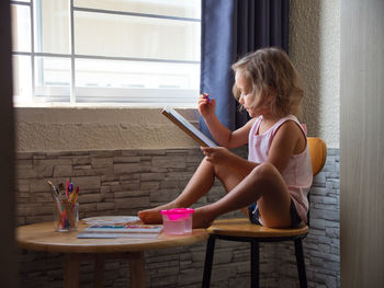 Girl drawing while sitting on stool at home