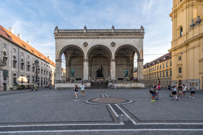 People on road by buildings in city against sky