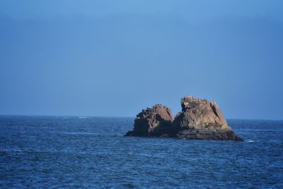 Rock formation in sea against clear blue sky