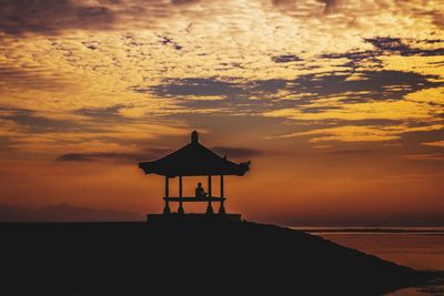 Silhouette house by sea against sky during sunset