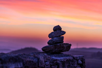 Stack of stones on rock against sky during sunset