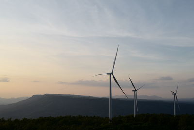 Wind turbines on landscape against sky during sunset