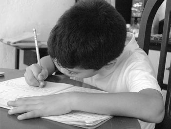 Boy writing in book while sitting on table