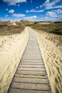 Surface level of boardwalk on land against sky