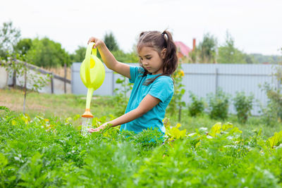 Little girl in a green t-shirt, watering a green bed of yellow watering can, in the garden