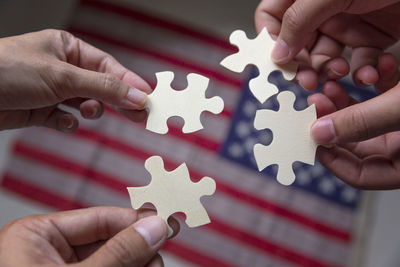 Cropped hands of people holding jigsaw pieces against american flag