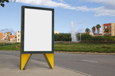 Empty road sign on street in city against sky