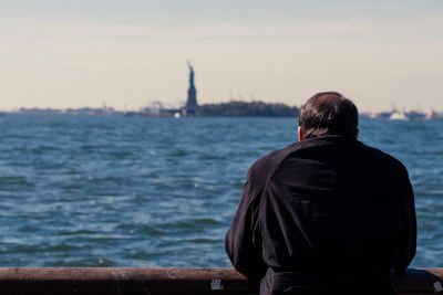 Rear view of man standing against river on sunny day in city