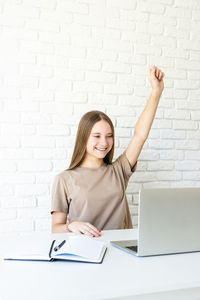 Portrait of smiling young woman using phone against wall