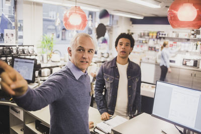 Male owner pointing while customer standing in background at electronics store