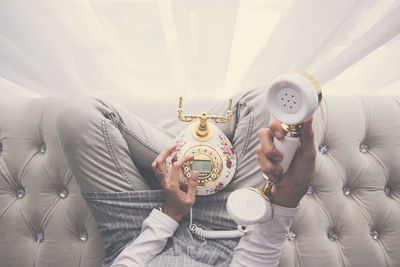 Midsection of woman holding telephone on sofa at home