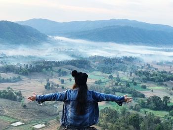 Rear view of young woman with arms outstretched standing on mountain against sky