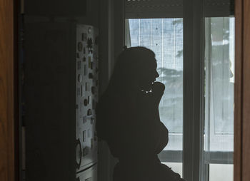 Silhouette woman standing by window at home