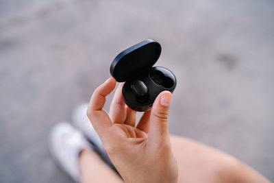 From above crop unrecognizable female holding power bank case with true wireless earbuds against blurred pavement