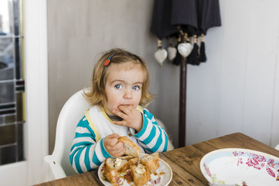 Portrait of girl eating food on table at home