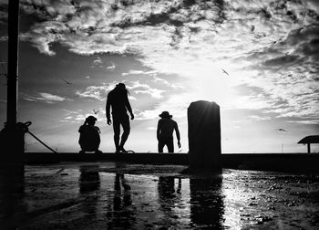 Silhouette people against sea against sky during sunset