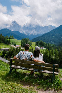 Rear view of people sitting on bench by mountains against sky