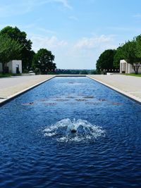 Swimming pool by trees against sky