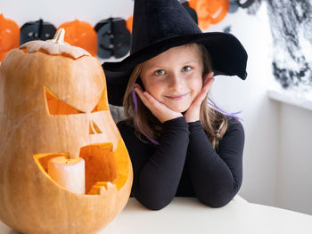 Cute girl in costume of witch with pumpkin at home, having fun, celebrating halloween