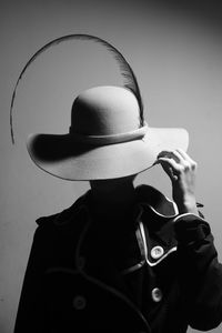 Close-up portrait of woman holding hat against wall