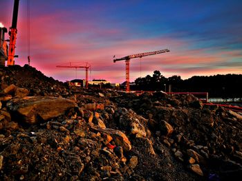 Cranes at construction site against sky during sunset