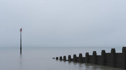 Wooden posts in sea against clear sky