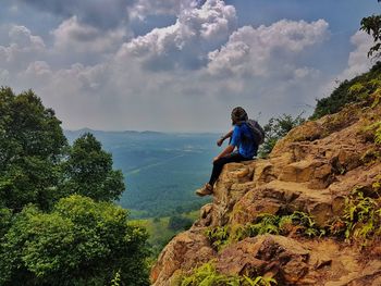 Side view of man sitting on cliff against sky