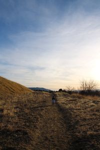 Rear view of girl walking on field against sky