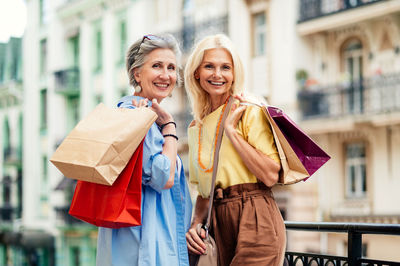 Portrait of smiling young woman holding shopping bags while standing in city