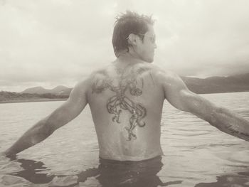 Rear view of shirtless man standing at beach against sky