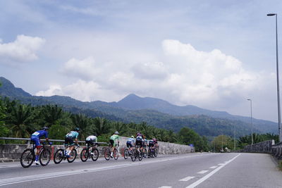 People riding bicycle on road against sky