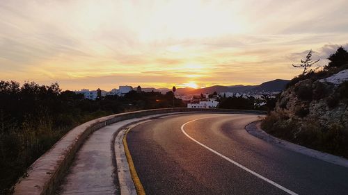 Road amidst trees against sky during sunset