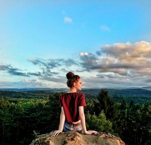 Rear view of young woman sitting on rock formation against sky during sunset