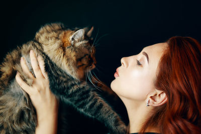 Young woman with cat against black background