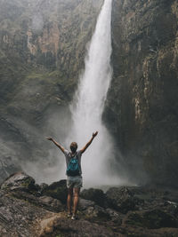 Rearview of a young woman opening arms while looking at the waterfall, queensland, australia.