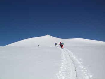 Rear view of people walking on snowcapped mountain against clear sky