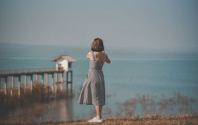 Rear view of woman standing at beach against sky