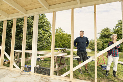 Serious couple looking at incomplete shed against trees