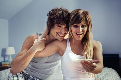 Cheerful couple with pregnancy test on bed at home