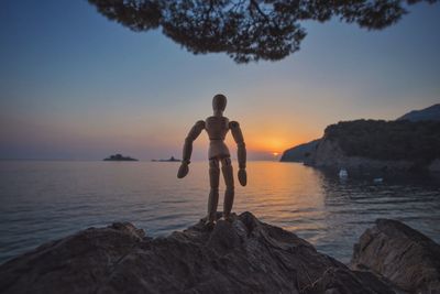 Man standing on rock by sea against sky during sunset