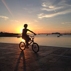 Silhouette man with bicycle on beach against sky during sunset